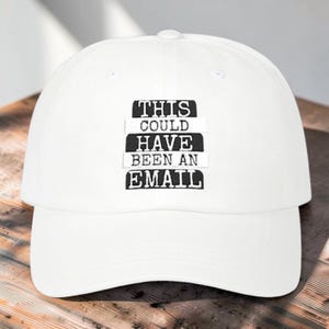 May include: A white baseball cap featuring black embroidered text on the front that reads THIS COULD HAVE BEEN AN EMAIL. The cap has a structured crown, a curved brim, and a button on the top centre, providing a clean and simple appearance.