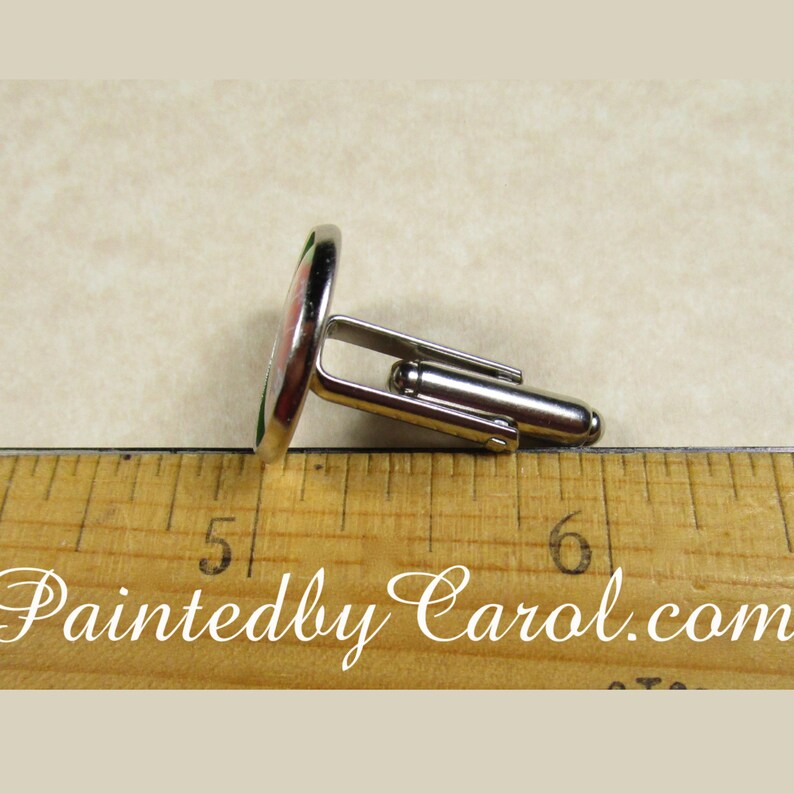 May include: A pair of silver cufflinks with a round, green, pink, and white design. The cufflinks are about 1.5 inches long and are shown next to a ruler.