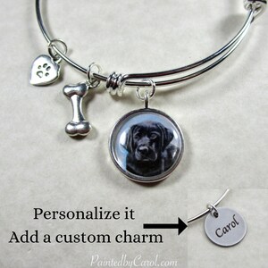 May include: Silver charm bracelet with a black Labrador Retriever charm, a bone charm, a paw print heart charm, and a blank charm that can be personalized with a name. The bracelet is shown with the name "Carol" on the blank charm.