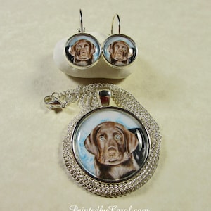 May include: A silver necklace and earrings set featuring a brown and white dog portrait. The necklace has a silver chain and a round pendant with a clear glass front. The earrings are silver hoops with a clear glass front.