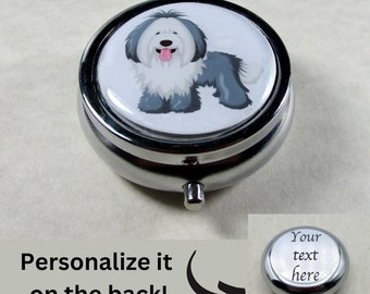 May include: A silver round pill box with a white lid featuring a cartoon Old English Sheepdog. The lid has a silver rim. The back of the pill box is plain silver and can be personalized with text.  The text "Your text here" is shown on the back of the pill box.