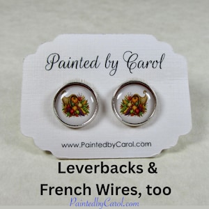 May include: A pair of round silver-tone stud earrings featuring a cornucopia graphic filled with colorful fruits and vegetables. The earrings are displayed on a white card with the text Painted by Carol and www.PaintedbyCarol.com.