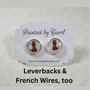 May include: A pair of silver earrings with a red Irish Setter dog image on each earring. The earrings are on a white card with the text "Painted by Carol" and "www.PaintedbyCarol.com". The text "Leverbacks & French Wires, too" is below the card. The text "PaintedbyCarol.com" is at the bottom of the image.