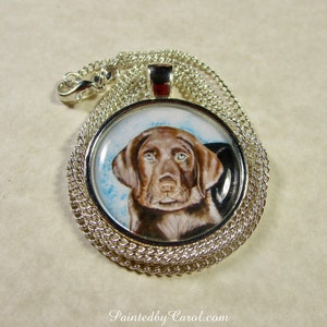 May include: A silver chain necklace with a round pendant featuring a hand-painted portrait of a chocolate brown Labrador Retriever puppy. The puppy has brown eyes and is looking directly at the viewer.