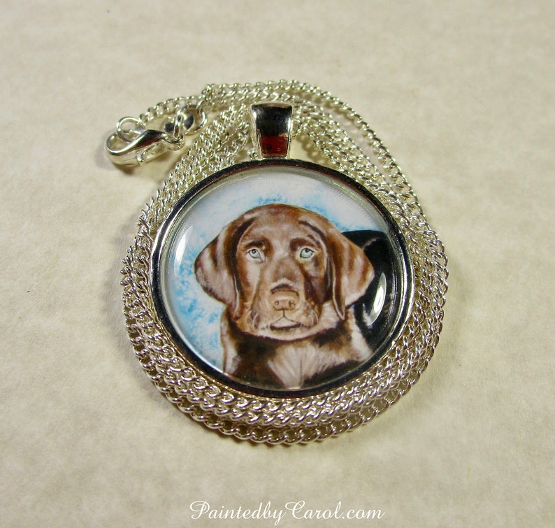 May include: A silver chain necklace with a round pendant featuring a hand-painted portrait of a chocolate brown Labrador Retriever puppy. The puppy has brown eyes and is looking directly at the viewer.