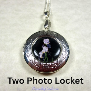 May include: Silver-toned, round locket pendant with a chain. The locket features a black background with a painting of purple and white irises. The text "Two Photo Locket" is below the pendant.