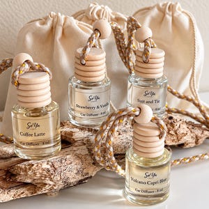 May include: Four 8 ml glass car diffuser bottles with light wood caps and braided hanging cords. Each bottle features a label with the So Ya Ember logo and scent names: Coffee Latte, Strawberry & Vanilla, Suit and Tie, and Volcano Capri Blue.