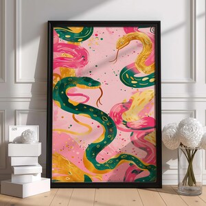 Könnte beinhalten: Ein gerahmter, rechteckiger Wandkunstdruck mit einer lebendigen Illustration mehrerer Schlangen in Grün-, Gold- und Rosatönen vor einem hellrosa Hintergrund. Die Schlangen sind mit strukturierten Mustern und sichtbaren Zungen dargestellt.