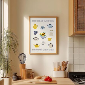 May include: A framed wall art print featuring a collection of illustrated teapots, teacups, and a sunflower bouquet. The text reads GOOD FOOD AND WARM KITCHEN IS WHAT MAKES A HOUSE A HOME. The design uses a palette of yellow, blue, and white colours.