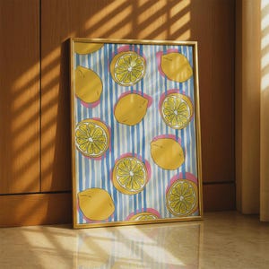 May include: A rectangular wall art print in a thin gold frame featuring a repeating pattern of yellow lemons and lemon slices on a background of vertical blue stripes with soft pink circular accents behind each lemon element.