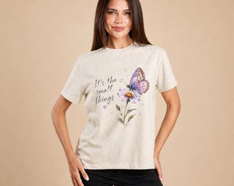May include: A light beige t-shirt featuring a watercolor illustration of a butterfly and a flower. The text "It's the small things" is printed on the shirt. The shirt is short-sleeved and has a crew neck.