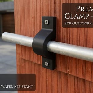 May include: A black premium pipe clamp, designed for 1/2 inch conduits, is mounted on a reddish-brown wooden surface. The clamp secures a silver pipe. Text on the image reads "PREMIUM PIPE CLAMP - 1/2 INCH FOR OUTDOOR & INDOOR CONDUITS". The clamp is UV and water resistant.
