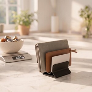 May include: A black metal desk organizer holding a gray wallet, a brown leather card holder, and a white card. A bowl of coffee pods sits on a scale, displaying 302.5g. The scene is set on a marble countertop with plants in the background.