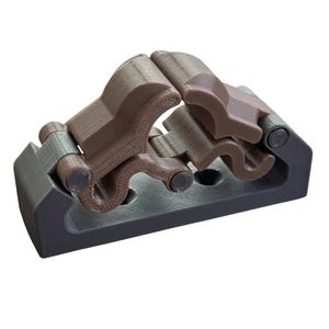 May include: A 3D-printed object with a dark gray base and brown upper components. The design features interlocking, curved shapes and cylindrical joints. The object appears to be a mechanical or structural component, possibly for a larger assembly.