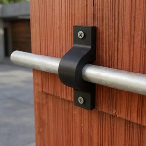 May include: A black metal bracket secures a silver metal rod to a reddish-brown wooden surface. The bracket is attached with two screws. The rod is horizontal, and the wood has a vertical grain.