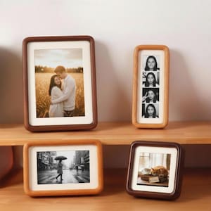 May include: A collection of wooden picture frames in various shapes and sizes. The frames display photographs of a couple, a series of portraits, a city scene, and a cat. The frames are made of wood with a natural finish.