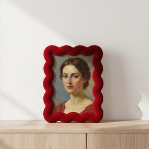May include: A portrait of a woman in a red velvet frame. The frame has a wavy, scalloped edge. The portrait features a woman with brown hair and a red dress. The background is a soft blue.