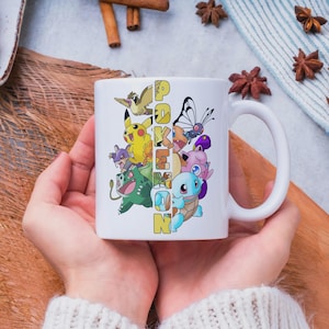 May include: White ceramic mug featuring a colorful design of various Pokemon characters and the word "Pokemon" in yellow and blue. The mug has a large handle and is held by a person wearing a white sweater. The mug is a perfect gift for fans of the popular franchise.