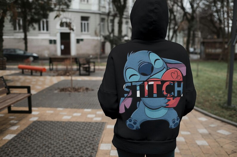 May include: Black hooded sweatshirt featuring a large graphic of the character Stitch from Lilo & Stitch. Stitch is blue with large ears, holding a red heart. The word "STITCH" is printed in white across the design.