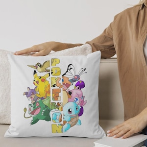 May include: White square pillow featuring a colorful graphic of various Pokemon characters, including Pikachu, Bulbasaur, and Squirtle. The word "Pokemon" is vertically printed in yellow and orange. The pillow is on a white couch.