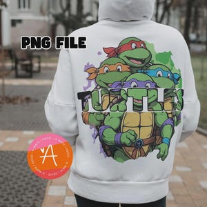 Puede incluir: Una sudadera con capucha blanca que presenta un gran gráfico en la espalda de cuatro tortugas de dibujos animados verdes con máscaras de colores. El texto "TURTLES" está impreso en letras negras en negrita en el centro del gráfico, sobre un fondo de estilo acuarela verde y morado.