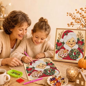 May include: A diamond painting kit featuring a smiling Mrs. Claus holding a tray of cookies and a green wreath. The design includes red, white, and green rhinestones. A pink stylus and a tray of colorful beads are visible on the table surface.