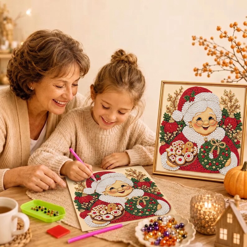 May include: A diamond painting kit featuring a smiling Mrs. Claus holding a tray of cookies and a green wreath. The design includes red, white, and green rhinestones. A pink stylus and a tray of colorful beads are visible on the table surface.