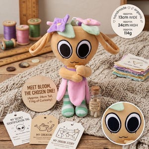Puede incluir: Una muñeca de peluche hecha a mano y orgánica, de aproximadamente 24 cm de alto y 13 cm de ancho, con grandes ojos negros, orejas caídas y adornos florales. La muñeca lleva un atuendo rosa y verde. La imagen incluye una etiqueta de madera que dice "MEET BLOOM, THE CHOSEN ONE!"