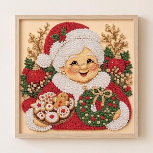 May include: A square framed diamond art piece depicting Mrs. Claus wearing a red hat and white fur trim, holding a plate of cookies and a green wreath. The image is composed of small, shiny beads in red, green, white, and gold, creating a textured effect.