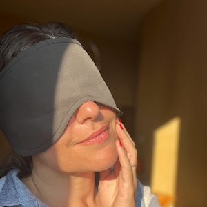 K&ouml;nnte beinhalten: Eine einfarbige, dunkelgraue Schlafmaske aus Stoff mit konturierter Form, die die Augen bedeckt. Die Maske hat eine glatte, matte Oberfl&auml;che und gen&auml;hte Kanten, was ein einfaches und funktionales Design bietet, um Licht w&auml;hrend des Schlafs abzuschirmen.