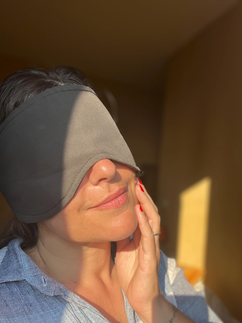 K&ouml;nnte beinhalten: Eine einfarbige, dunkelgraue Schlafmaske aus Stoff mit konturierter Form, die die Augen bedeckt. Die Maske hat eine glatte, matte Oberfl&auml;che und gen&auml;hte Kanten, was ein einfaches und funktionales Design bietet, um Licht w&auml;hrend des Schlafs abzuschirmen.