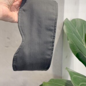 K&ouml;nnte beinhalten: Eine dunkelgraue Schlafmaske mit konturierter Form, die &uuml;ber die Augen passt. Die Maske weist sichtbare N&auml;hte entlang der R&auml;nder und eine glatte, matte Stoffoberfl&auml;che auf. Es ist ein schlichtes, funktionales Accessoire zur Lichtabschirmung.