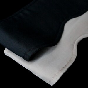 K&ouml;nnte beinhalten: Nahaufnahme von zwei Schlafmasken, eine schwarze und eine wei&szlig;e, die sich vor einem schwarzen Hintergrund &uuml;berlappen. Die schwarze Maske scheint aus einem glatten, satinartigen Material zu bestehen, w&auml;hrend die wei&szlig;e Maske eine strukturierte Stoffoptik hat.