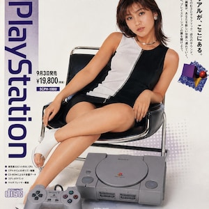 Może przedstawiać: Zabytkowa reklama Sony PlayStation przedstawiająca szarą konsolę do gier i kontroler, model SCPH-1000, z japońskim tekstem, ceną 19 800 jenów oraz małymi zrzutami ekranu z gier, takich jak Ridge Racer Type 4, Tekken 3, Parasite Eve i Metal Gear Solid.
