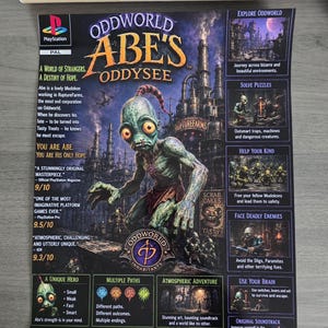 May include: A rectangular poster for the PlayStation game Oddworld: Abe's Oddysee, featuring the green-skinned character Abe in the center, surrounded by game text, screenshots, and the PlayStation logo, rolled inside a brown cardboard tube.