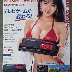 May include: SEGA Master System advertisement from 1985. The image features a woman holding the black and red console. The ad includes text in Japanese, showcasing the console's features and available games.