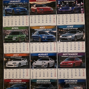 May include: A 2027 wall calendar titled JDM CARS 2027 featuring twelve monthly pages. Each month displays a different Japanese sports car, including models like the Nissan Skyline, Toyota Supra, Mazda RX-7, and Mitsubishi Lancer Evolution.