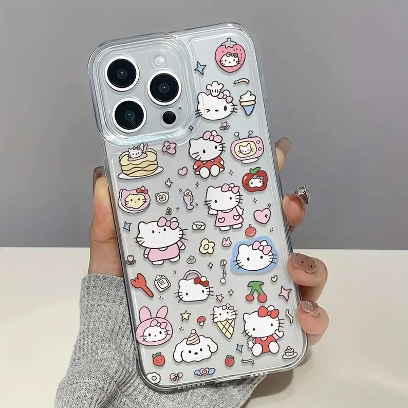 May include: Clear phone case decorated with colorful Hello Kitty character stickers. The stickers include Hello Kitty in various outfits, food items, and other cute designs. The case is held in a hand.