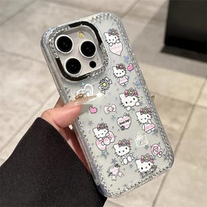 May include: Clear phone case with a sparkly, glittery design. The case features a pattern of Hello Kitty characters, pink hearts, bows, and stars. The edges are lined with small, clear rhinestones. The text "Good day!" and "Hello" are visible.
