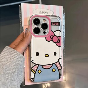Pode incluir: Capa de telefone transparente com um personagem de gato de desenho animado com um la&ccedil;o rosa e macac&atilde;o azul. A capa tem uma borda rosa ao redor da c&acirc;mera e a palavra "LOVE" &eacute; impressa na capa e na embalagem.