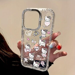 May include: Clear phone case with a silver frame and a sparkling rhinestone border. The case features multiple Hello Kitty illustrations in various poses, along with hearts, bows, and flowers. The words "Hello" are visible at the bottom.