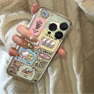 May include: Clear phone case with colorful stickers featuring cartoon characters, flowers, and text. The case has a clear border and a multi-lens camera cutout. The stickers are in shades of pink, blue, and yellow.