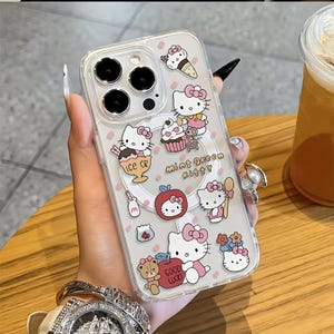 May include: Clear phone case with a colourful design featuring the character Hello Kitty, ice cream, cupcakes, and apples. The case has the words "Mint Green Kitty" and "Good Luck" printed on it. The case is held by a person.