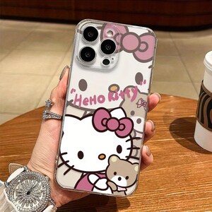 Puede incluir: Funda transparente para tel&eacute;fono con dise&ntilde;o de Hello Kitty, lazo rosa y osito de peluche. La funda tiene el texto "Hello Kitty" en rosa. Dise&ntilde;ada para un smartphone.