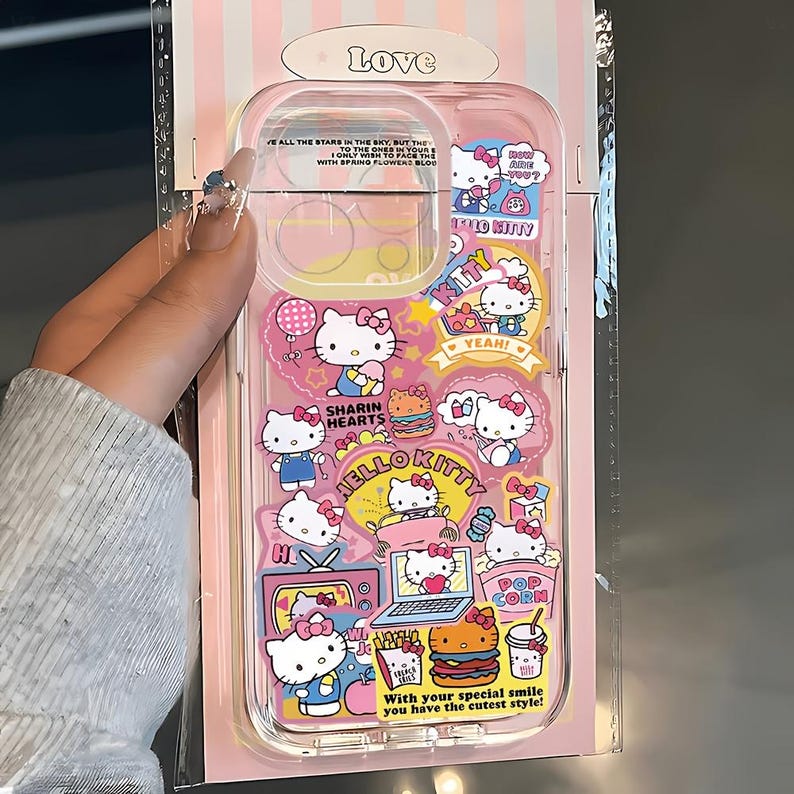 May include: Clear phone case with a pink and white striped background. The case features Hello Kitty graphics and text, including "Hello Kitty", "Yeah!", and "With your special smile you have the cutest style!"