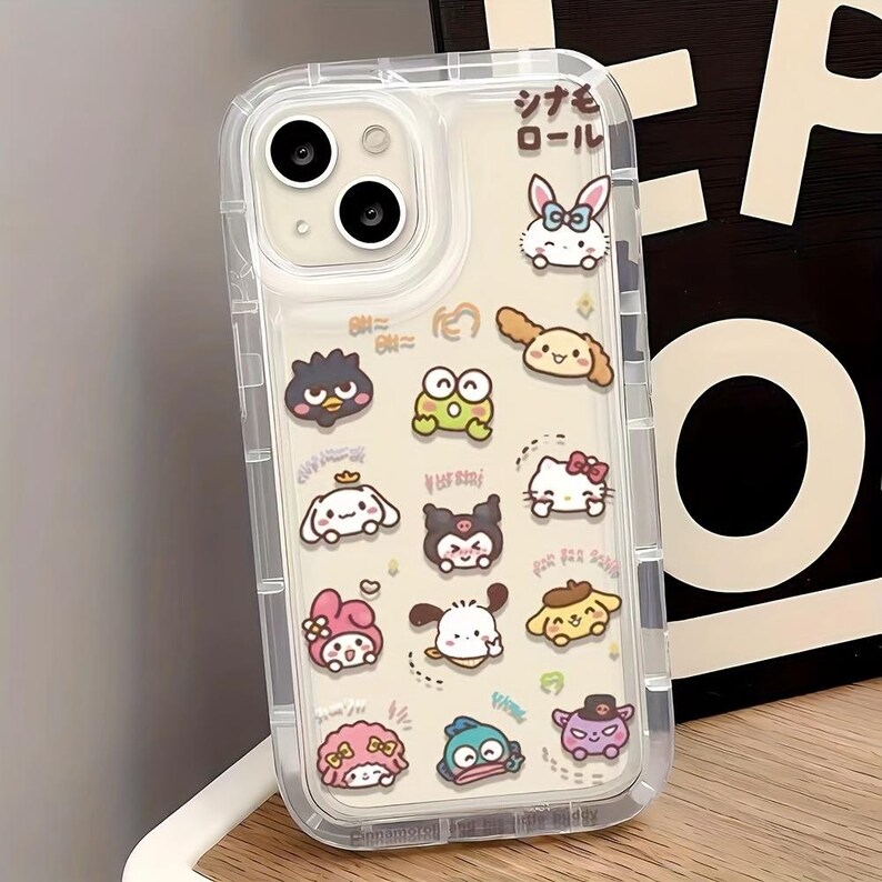 Puede incluir: Carcasa transparente para tel&eacute;fono con un dise&ntilde;o colorido que presenta varios personajes de dibujos animados, incluyendo Hello Kitty, My Melody y Kuromi. La carcasa tiene un borde elevado alrededor del objetivo de la c&aacute;mara y una parte posterior transparente.