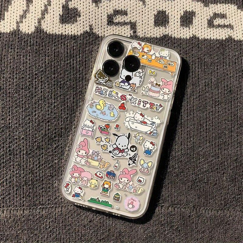 May include: Clear phone case decorated with colorful cartoon character stickers. The case features a variety of designs, including Hello Kitty, ducks, and other cute illustrations. The case has a clear back and black camera lenses.