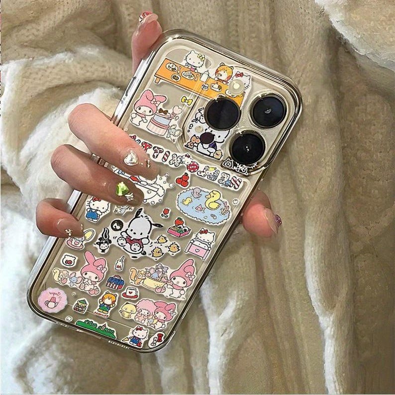 May include: Clear phone case decorated with colorful cartoon character stickers. The case has a clear back and a transparent border. The stickers feature various characters and designs, including Hello Kitty and My Melody.