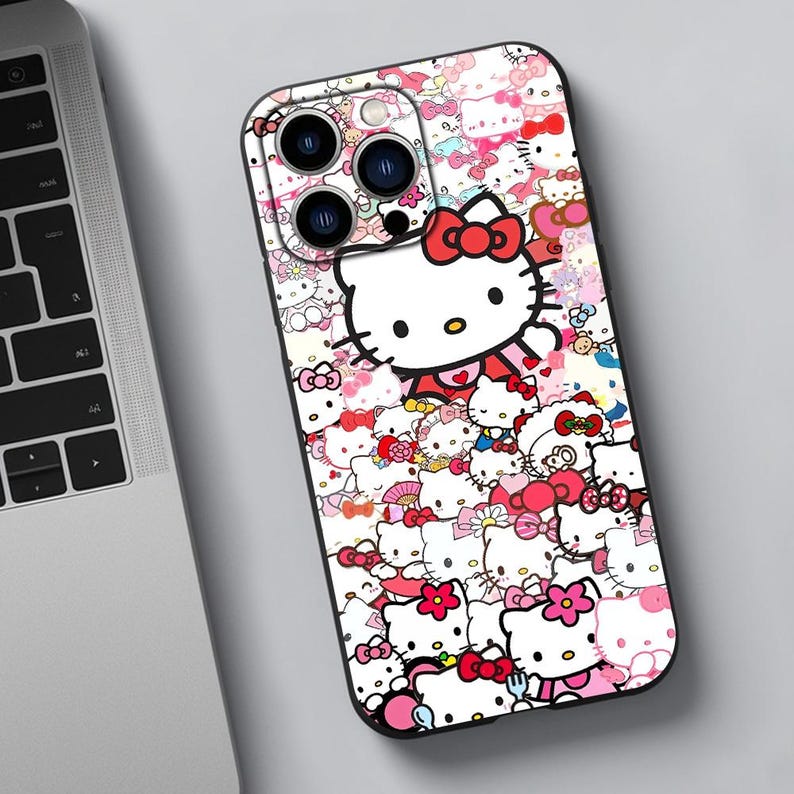 May include: A black phone case with a colorful design featuring Hello Kitty and other characters. The case has a camera cutout and a white background.