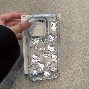May include: Clear phone case with a glittery border and a design featuring Hello Kitty characters, hearts, bows, and flowers. The case has the word "instagra" printed on it.